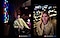 Two portraits in low-light conditions. First portrait taken with night mode: A person seated indoors by a table, with colorful stained glass windows in the background. Second portrait taken with portrait mode in low-light condition: A person standing outdoors at night, with a backdrop of soft, blurred city lights. Text reads Captured by Galaxy A55 5G #withGalaxy.